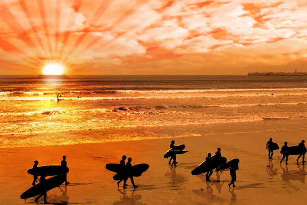 Surfers περπάτημα στην ένδοξη παραλία ηλιοβασίλεμα — Φωτογραφία Αρχείου