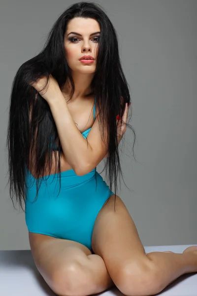 Приваблива сексуальна брюнетка в бірюзовому купальнику на сірому фоні — стокове фото