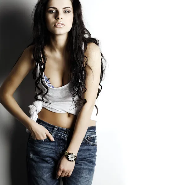 Portrait of beautiful sexual girl in jeans, standing near a white wall, in fashion style, glamur — Stock Photo, Image
