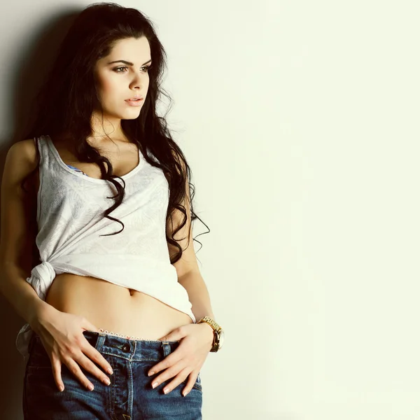 Portrait of beautiful sexual girl in jeans, standing near a white wall, in fashion style, glamur — Stock Photo, Image