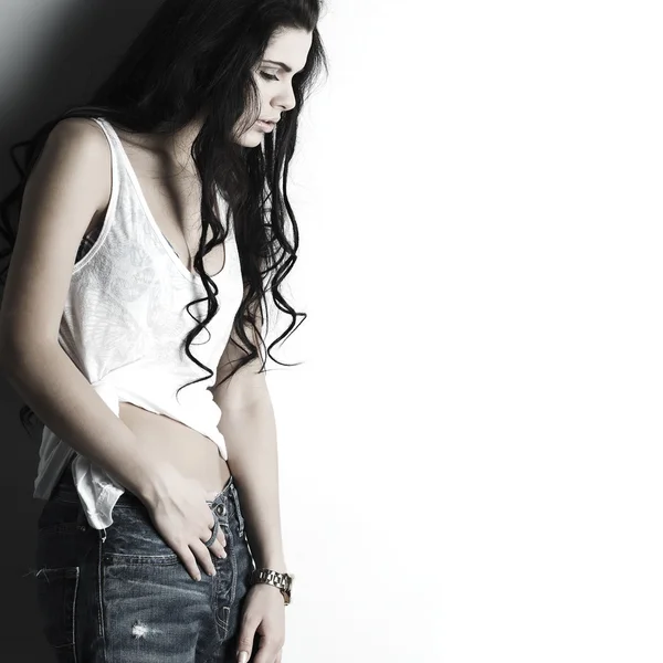 Retrato de hermosa chica sexual en jeans, de pie cerca de una pared blanca, en estilo de moda, glamur —  Fotos de Stock