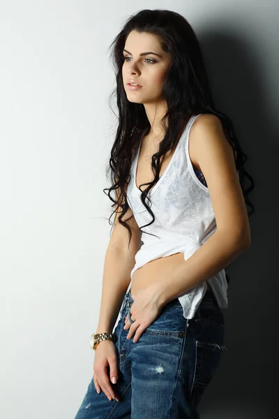 Retrato de hermosa chica sexual en jeans, de pie cerca de una pared blanca, en estilo de moda, glamour — Foto de Stock