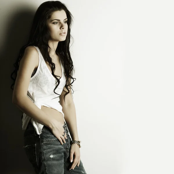 Портрет красивої сексуальної дівчини в джинсах, що стоїть біля білої стіни, в стилі моди, гламур — стокове фото