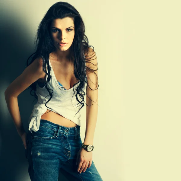 Portrait of beautiful sexual girl in jeans, standing near a white wall, in fashion style, glamour — Stock Photo, Image
