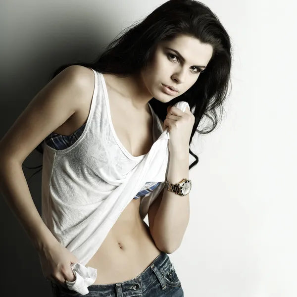 Retrato de hermosa chica sexual en jeans, de pie cerca de una pared blanca, en estilo de moda, glamour —  Fotos de Stock