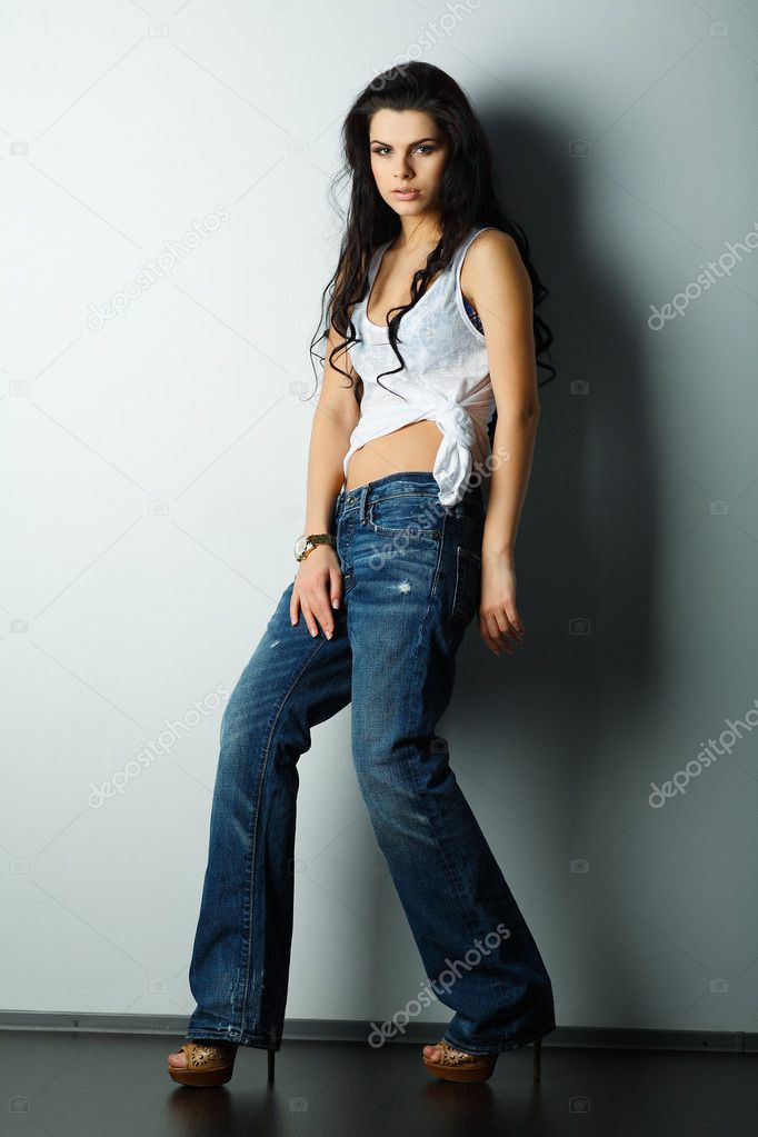 Portrait of beautiful sexual girl in jeans, standing near a white wall, in fashion style, glamour
