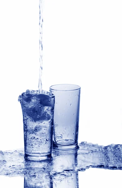 A glass is overfilled with water and an empty glass — Stock Photo, Image