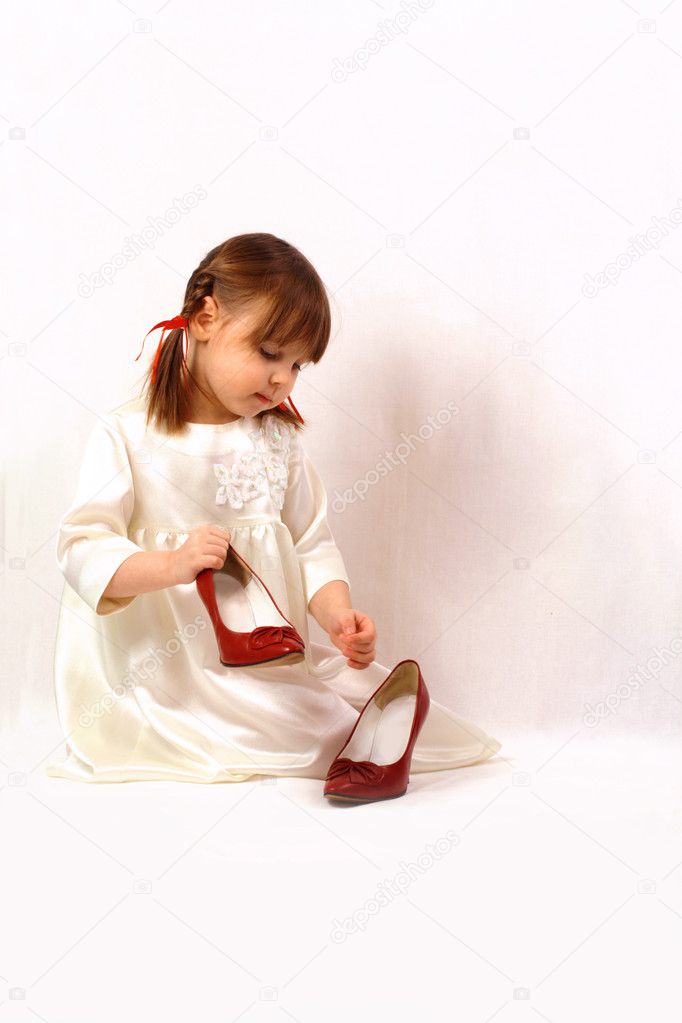 A little girl plays with big shoes