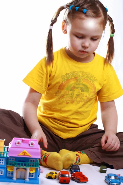 Uma menina brinca com carros de brinquedo e casas — Fotografia de Stock