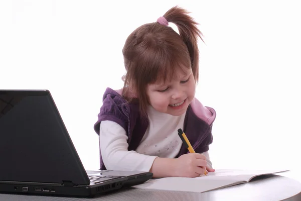 Маленькая девочка сидит рядом с ноутбуком и рисует ручкой — стоковое фото