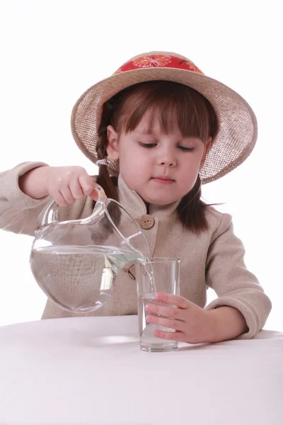 Ein kleines Mädchen gießt Wasser aus einem Krug in ein Glas — Stockfoto