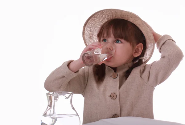 A little girl sits and drinks water from a glass — Zdjęcie stockowe