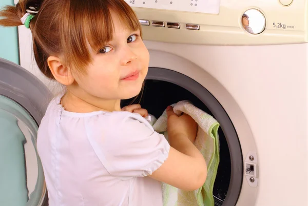Маленькая девочка кладет полотенца в стиральную машину — стоковое фото