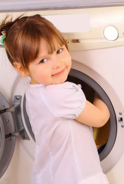 Küçük bir kız havlu çamaşır makinesine koyar. Stok Resim