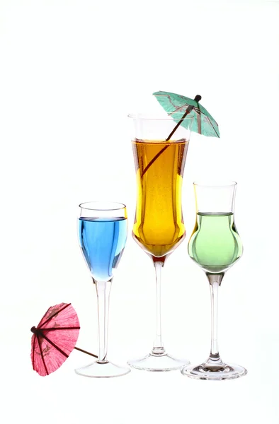 Τρία ποτηράκια μιας γεμίζουν με τα χρωματισμένα ποτά και κοκτέιλ ομπρέλες Royalty Free Φωτογραφίες Αρχείου