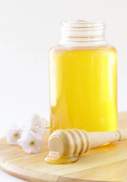 Miel fresca dorada en tarro con una cuchara de madera y flores —  Fotos de Stock