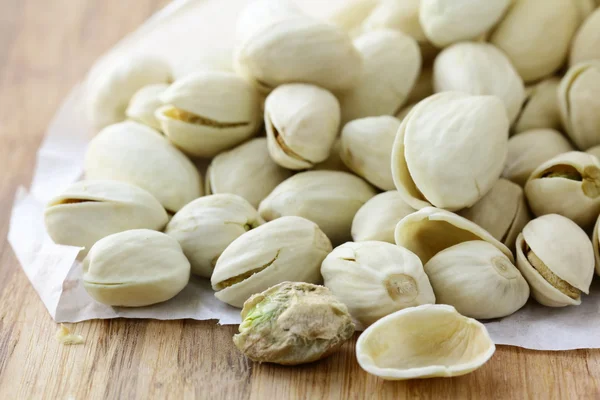 Nueces de pistacho en una cáscara blanca sobre una tabla de madera —  Fotos de Stock