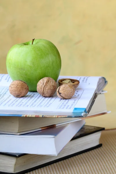 Zelená jablka a ořechy na hromadě knih — Stock fotografie