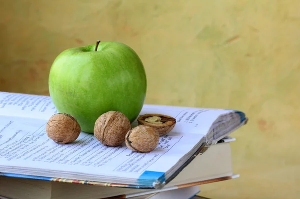 Groene apple en walnoten op een stapel boeken — Stockfoto