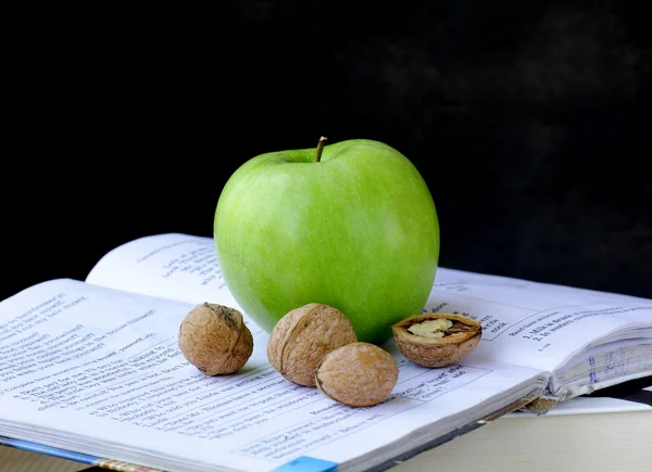 Green apple and walnuts on a pile of books — Stock Photo, Image