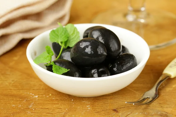 Marynowane oliwki czarne w misce na drewnianym stołem — Zdjęcie stockowe