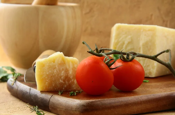 Parmesão de queijo em uma tábua de madeira com tomates — Fotografia de Stock