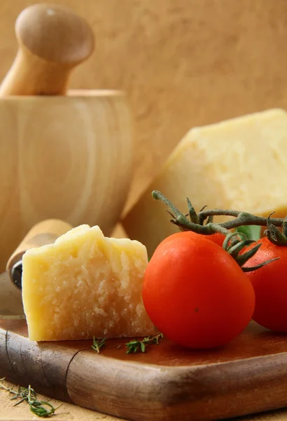 Queso parmesano sobre una tabla de madera con tomates —  Fotos de Stock