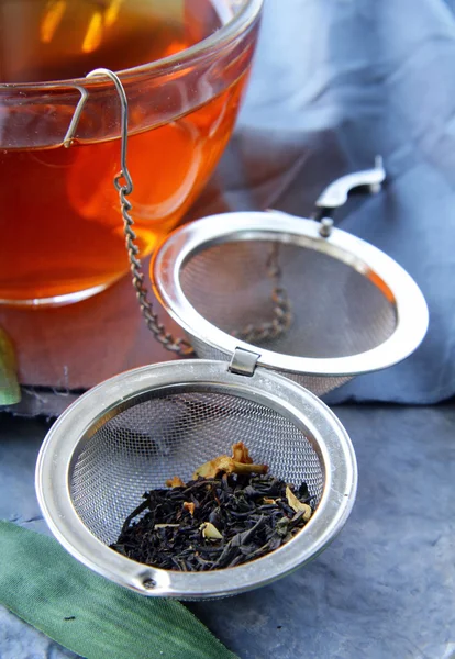 Tea strainer with a fragrant black tea and cups in the background — Stock Photo, Image