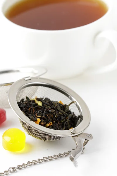 Tea strainer with a fragrant black tea and cup in the background — Stock Photo, Image