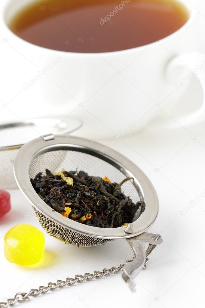 Tea strainer with a fragrant black tea and cup in the background