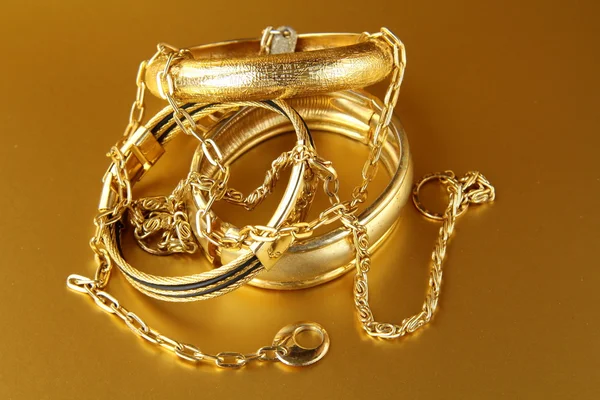 Золотые украшения, браслеты и цепочки на золотом фоне — стоковое фото