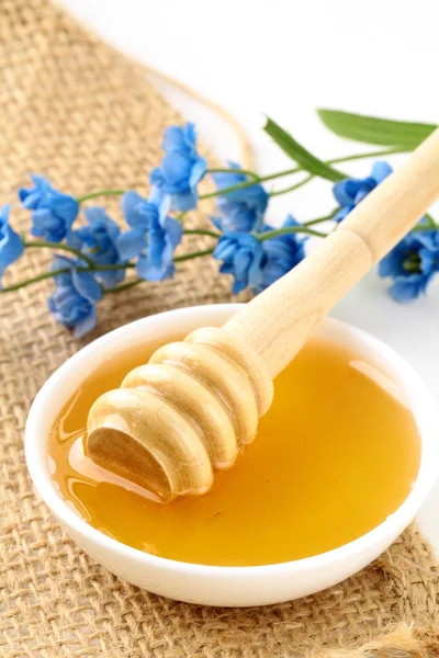 Fresh golden honey in jar with a wooden spoon and flowers — Stock Photo, Image
