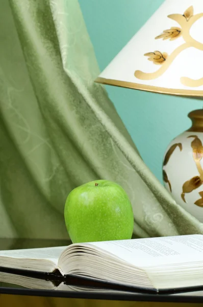 Buch mit Apfel auf Schreibtisch auf grünem Hintergrund — Stockfoto