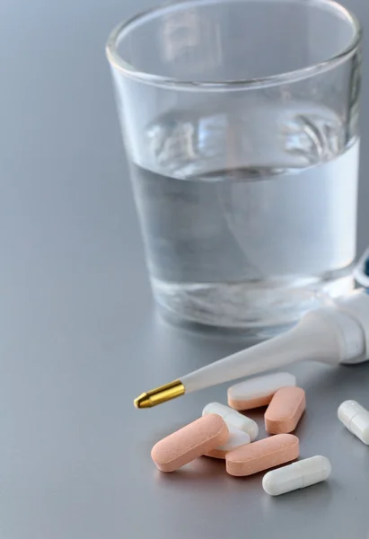 Electronic thermometer, pills and glass with water — Stock Photo, Image