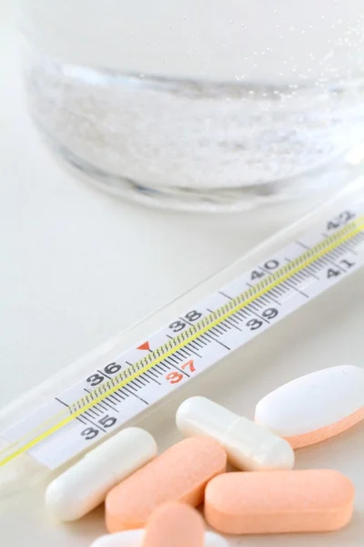Thermometer, pills and glass with water — Stock Photo, Image