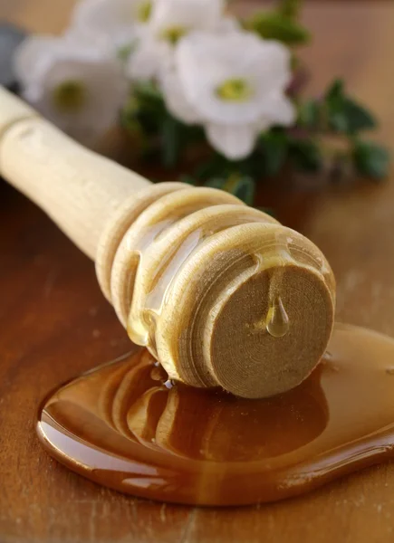 Miel fresca dorada con una cuchara de madera y flores — Foto de Stock