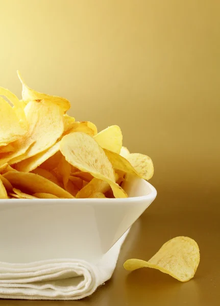 Картофельные чипсы в белой миске на золотом фоне — стоковое фото