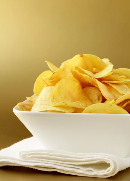 Potato chips in a white bowl on a gold background — Stock Photo, Image