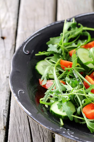 Salad with arugula and cherry tomatoes on black vintage plate — Stock Photo, Image