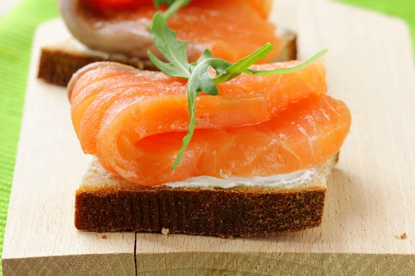 Сэндвич с копченым лососем и рукколой на деревянной доске — стоковое фото