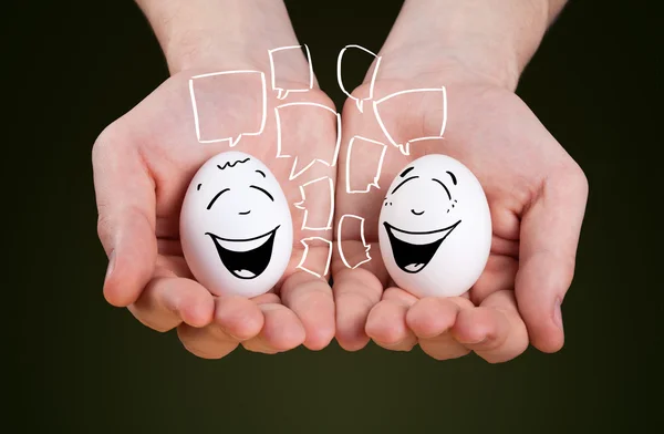 Mano masculina sosteniendo huevos con caras sonrientes — Foto de Stock