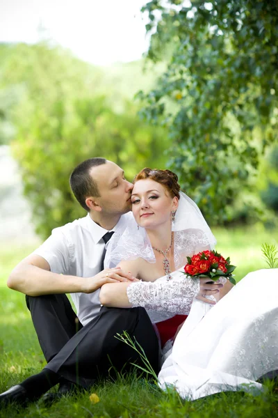 Bruid en bruidegom zittend op het gras — Stockfoto