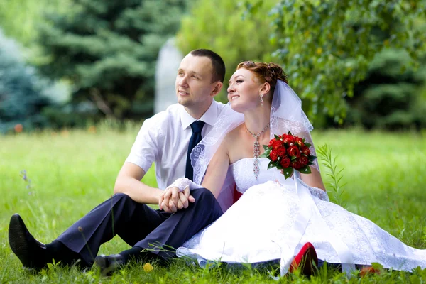 Bride and groom sitting on the grass — Stock Photo, Image