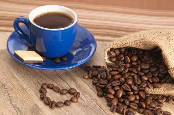 Cup of coffee with beans on old wooden surface — Stock Photo, Image