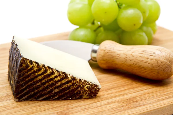 Manchego cheese ang grapes on chopping board — Stock Photo, Image