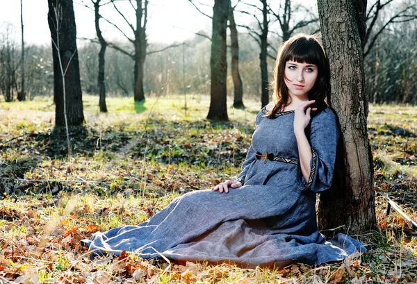 Молодая женщина в средневековом платье сидит рядом с деревом — стоковое фото