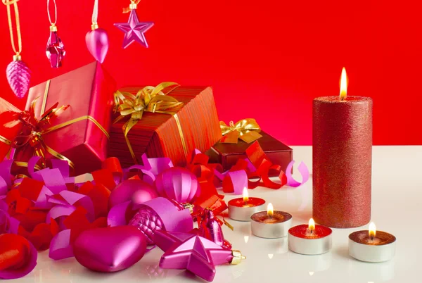 Weihnachtsgeschenke mit Kerzen auf rotem Hintergrund — Stockfoto