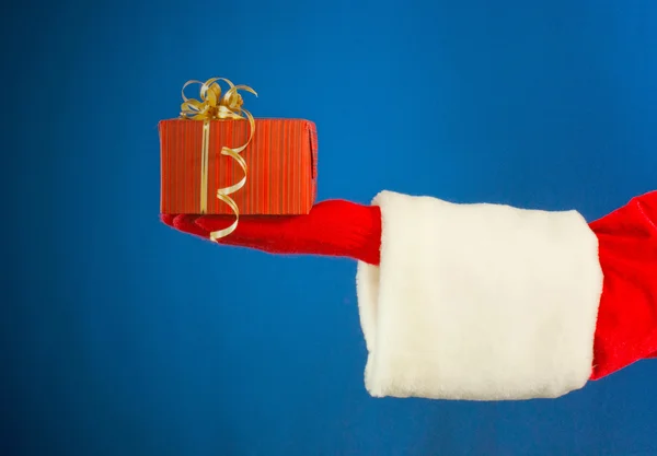 Mão do Papai Noel segurando um presente sobre fundo azul — Fotografia de Stock