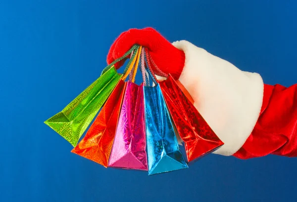 Mão do Papai Noel segurando sacos coloridos — Fotografia de Stock
