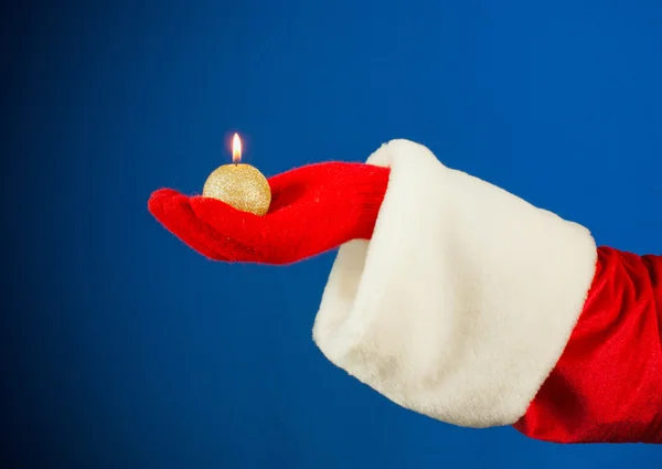 Mão do Papai Noel segurando uma vela acesa sobre fundo azul — Fotografia de Stock